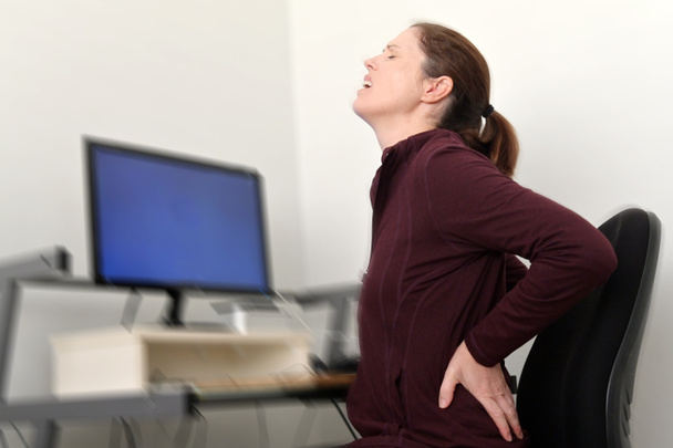 La donna che lavora su un computer in un ufficio domestico soffre di mal di schiena. - Foto, immagini