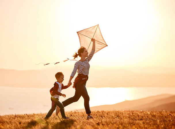 Gelukkige familie moeder en kind zoon lanceren een vlieger op de natuur bij zonsondergang - Foto, afbeelding