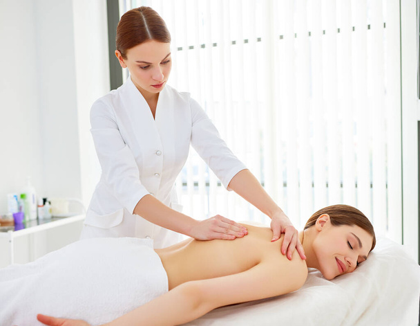 Young happy woman enjoying classic back massage by professional female therapist or masseur, relaxing with closed eyes in beauty salon or spa center. Beauty treatment and healthy lifestyle concept - Zdjęcie, obraz