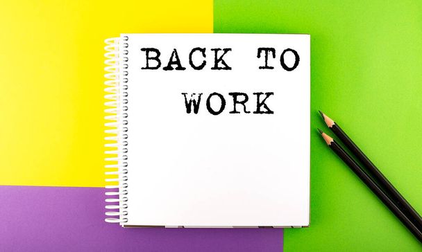 Espaço mínimo de trabalho: caderno de esboços sobre o fundo colorido com VOLTAR AO TRABALHO - Foto, Imagem