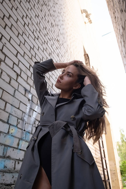 attractive asian model in trench coat standing near walls shot from lower point - Foto, afbeelding