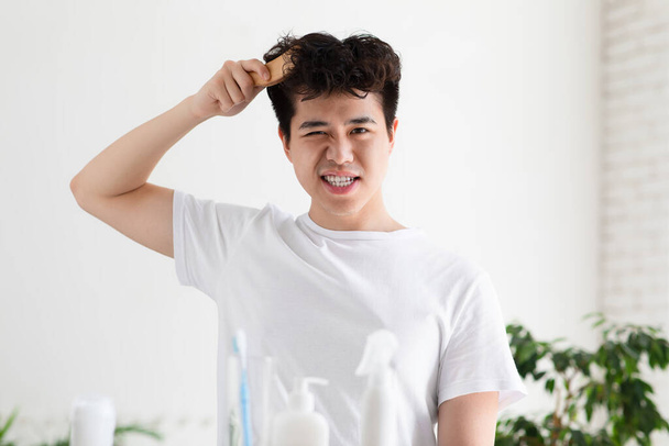 asiático guapo joven chico en blanco camiseta es combinando con cepillo - Foto, Imagen