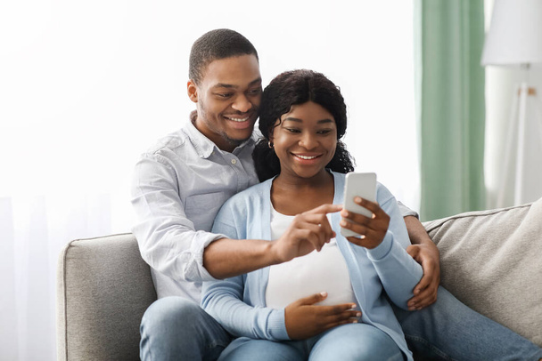 Loving black expecting parents shopping online, using smartphone - Photo, image