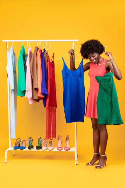 スタイリッシュなアフリカ系アメリカ人女性ショッピング選択ドレス、黄色の背景、垂直 - 写真・画像