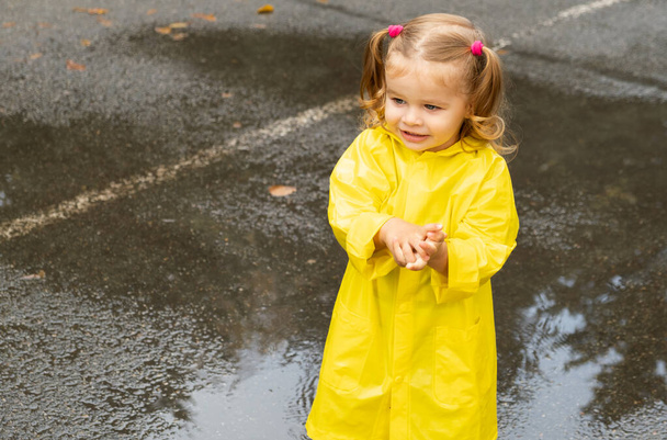 Schattig blond meisje peuter draagt gele stijlvolle regenjas close-up. kindertijd - Foto, afbeelding