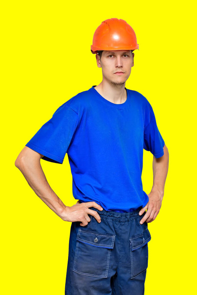 Portret młodego chudego pracownika w hełmie budowlanym i niebieskiej koszulce. Budowniczy lub wykonawca - Zdjęcie, obraz