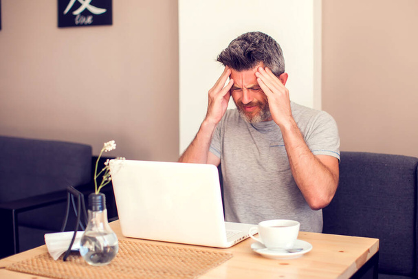Man having a headache in front of laptop. People, health care and technology concept - Fotó, kép