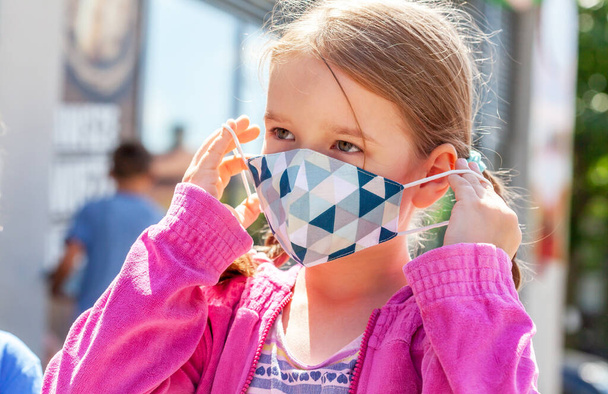 Okul çağındaki çocuk, renkli koruyucu tıbbi antiviral yüz maskesini takan ya da takan küçük kız açık hava portresi, yüz kapama, bahar, yaz. Corona virüsü, covid 19 çocuk koruması - Fotoğraf, Görsel