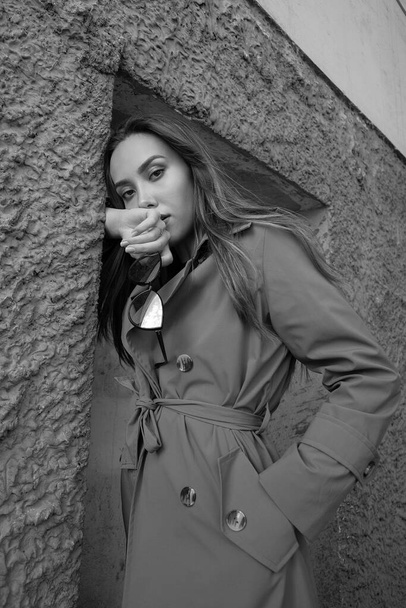 attractive asian model in trench coat standing near wall shot from lower point - Photo, Image