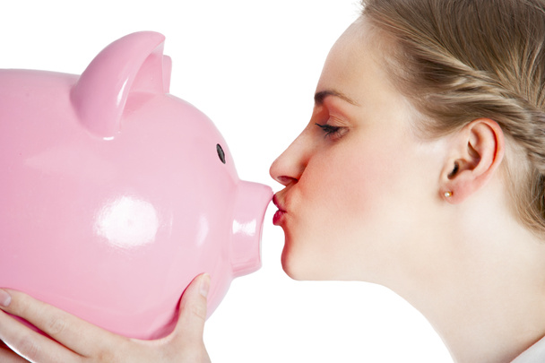 Blond young woman kissing a piggy bank with her lips - Foto, Bild