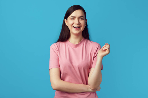 Young lady in pink tshirt smiling and standing with hands crossed on yellow - Foto, afbeelding