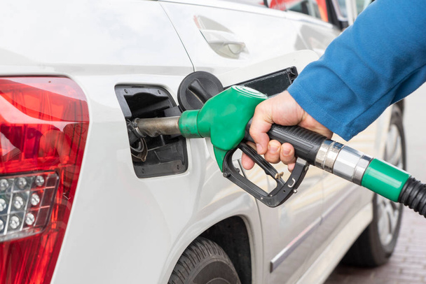 La mano dell'uomo tiene pompa di gas verde nel serbatoio dell'auto durante il processo di rifornimento dell'auto con benzina o diesel. Concetto di rifornimento - Foto, immagini