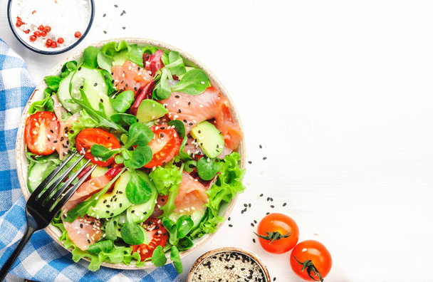 Fresh salmon salad with avocado, cucumber, sesame seeds, olive oil, tomatoes and mixed herbs. White background, top view - Foto, afbeelding