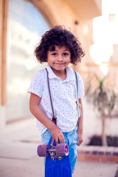 Niño pequeño con el pelo rizado con monopatín al aire libre. Niños y concepto de entretenimiento - Foto, Imagen