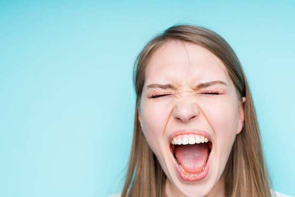 Beautiful girl with blond hair closes her eyes and screams with her mouth wide open - 写真・画像
