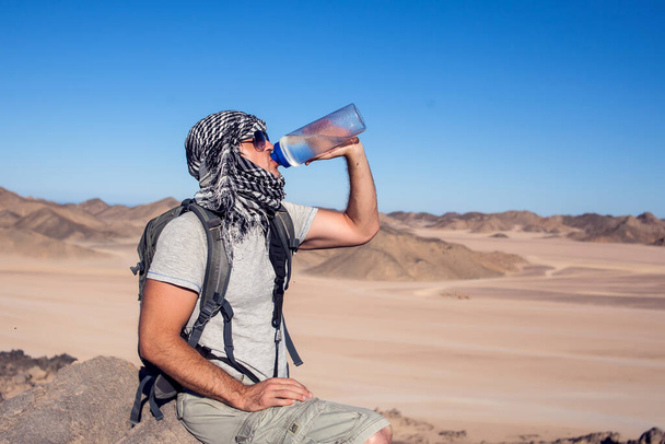 Чоловік відчуває спрагу і п'є воду в пустелі
. - Фото, зображення