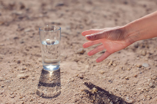 Una persona cerca di prendere un bicchiere d'acqua nel deserto. concetto di sete, calore e siccità - Foto, immagini