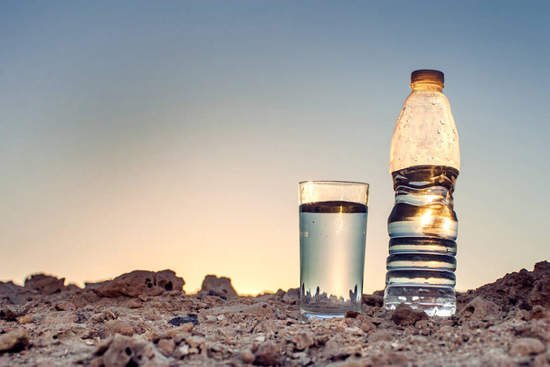 Sklo a láhev vody na písku v poušti. Žízeň, horko a sucho koncepce - Fotografie, Obrázek