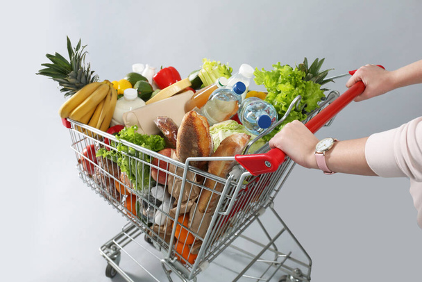 Woman with shopping cart full of groceries on grey background, closeup - Foto, Bild