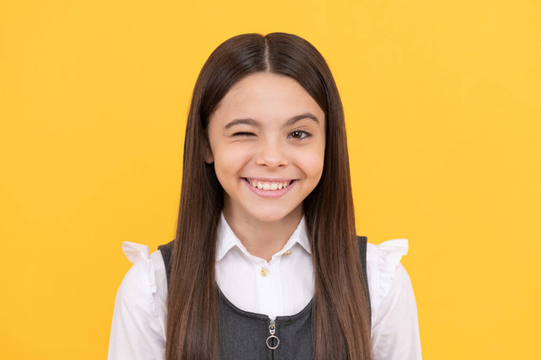 Happy school age girl child with smiling face give wink yellow background, winking - Photo, Image