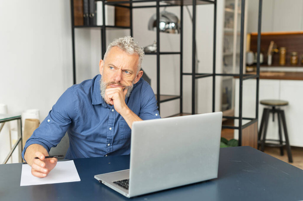 Απορροφημένη σκεπτικός ανώτερος επιχειρηματίας σε smart casual πουκάμισο κάθεται στο γραφείο - Φωτογραφία, εικόνα