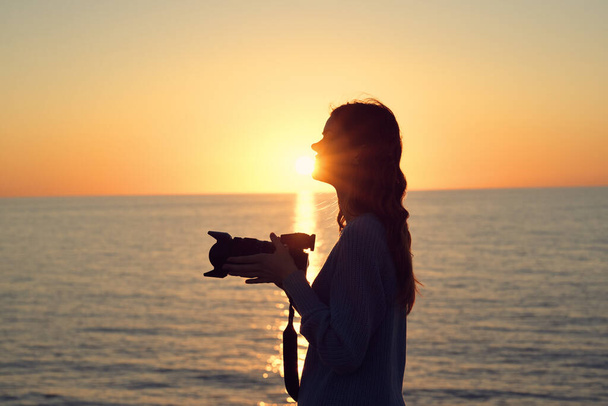 silueta de una mujer con una cámara al atardecer cerca de la vista al mar - Foto, imagen