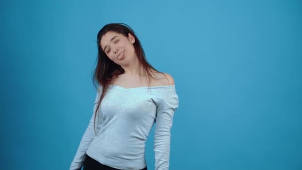 El retrato de una chica optimista y sonriente que muestra su lengua y sacude la cabeza juguetonamente. Asiática de pelo oscuro, vestida con blusa azul, aislada sobre fondo azul oscuro en el estudio. El - Imágenes, Vídeo