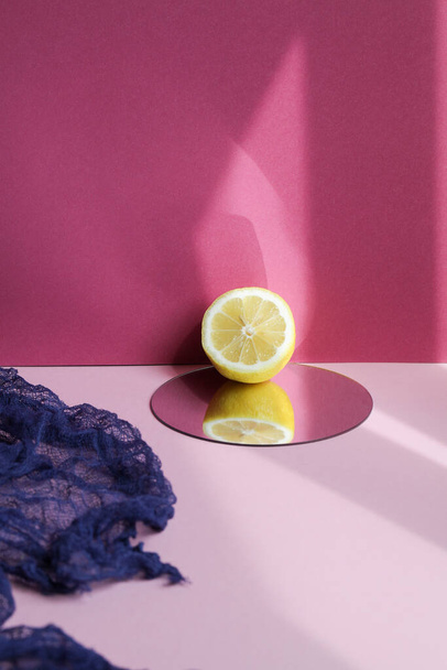 Minimal sunny fruit composition with dark blue fabric, lemon and mirror on purple background with sharp shadows. - Photo, image