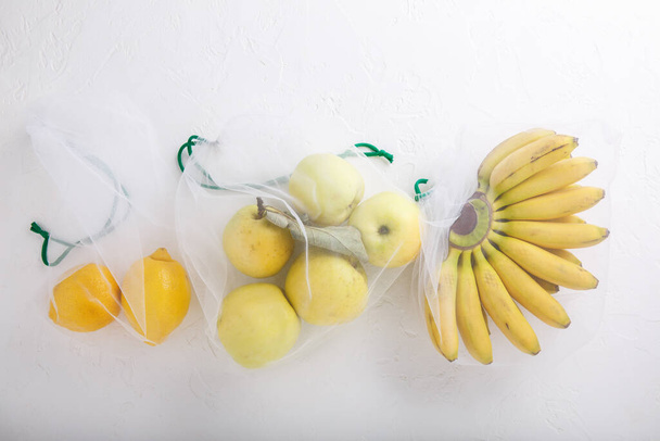 Banán, alma és citrom textilipari zsákokban. Sárga gyümölcsök és zöldségek újrahasznosítható környezetbarát csomagolásban, fehér alapon. Zéró hulladék vásárlás, műanyagmentes, szennyeződés megállítása, ökológiai koncepció.  - Fotó, kép