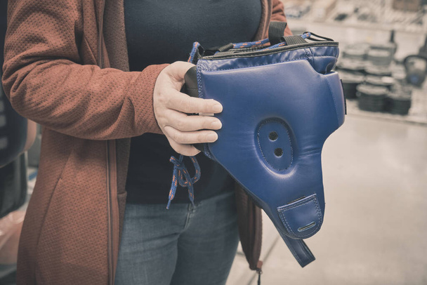 Mağazadaki kadın, boks sırasında kafanızı korumak için mavi kask almayı seçiyor. - Fotoğraf, Görsel