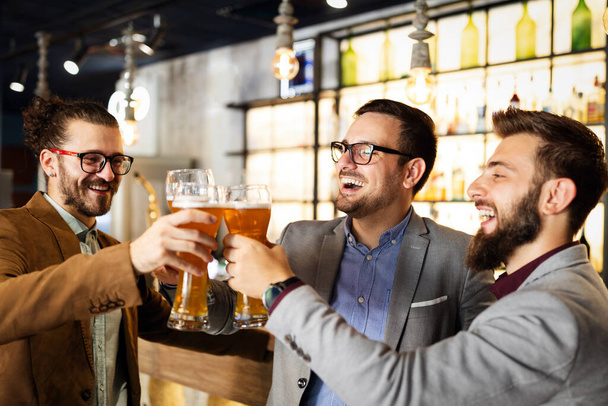 Young businessmen are drinking beer, talking and smiling while resting at pub - Foto, Imagem