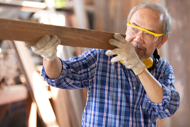 sênior asiático homem carpinteiro segurando e apontando madeira prancha no carpintaria oficina - Foto, Imagem