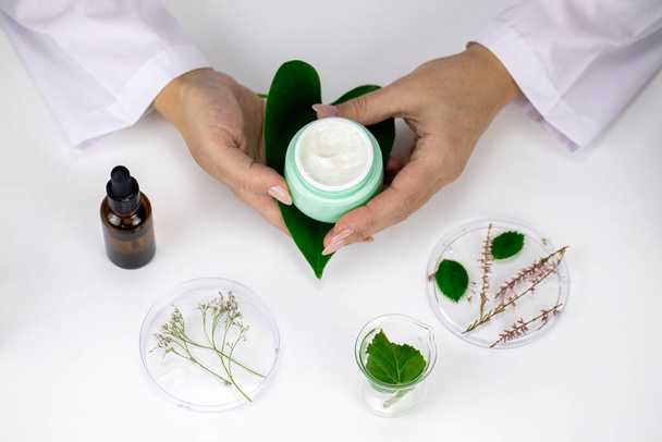 cosmetóloga manos femeninas sostienen la cara y la mano crema nutritiva en frasco verde abierto - Foto, imagen