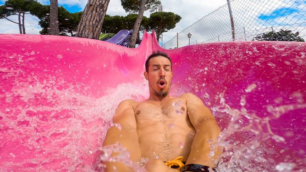 Селфи кавказца 40-х годов, мчащегося вниз по очень быстрому скольжению в розовой водной горке на летних каникулах. Развлечения в аквапарке во время летних каникул в Испании.. - Фото, изображение