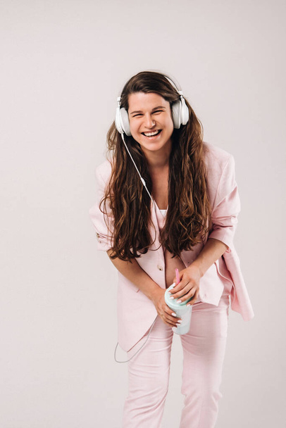 a pregnant woman in a pink suit with headphones emotionally listens to music on a gray background - Foto, Imagem
