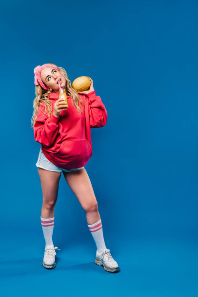 pregnant girl in pink clothes with a bottle of juice and a melon on a blue background - Photo, image