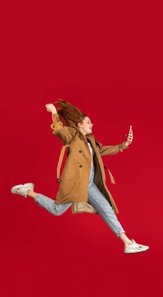 Young happy girl jumping isolated over red studio background with copyspace for ad. Concept of beauty, fashion. - Фото, изображение