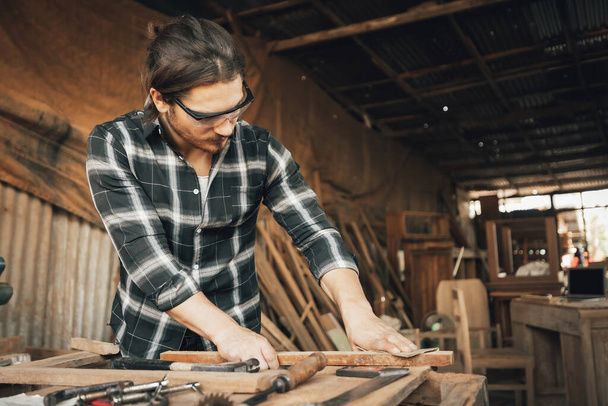 αρσενικό ξυλουργός χρησιμοποιώντας γυαλόχαρτο σε ένα κομμάτι ξύλου στο εργαστήριο (vintage τόνος) - Φωτογραφία, εικόνα