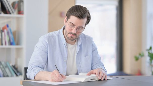 Gözlüklü Adam Kitap okuyor ve not alıyor.  - Fotoğraf, Görsel