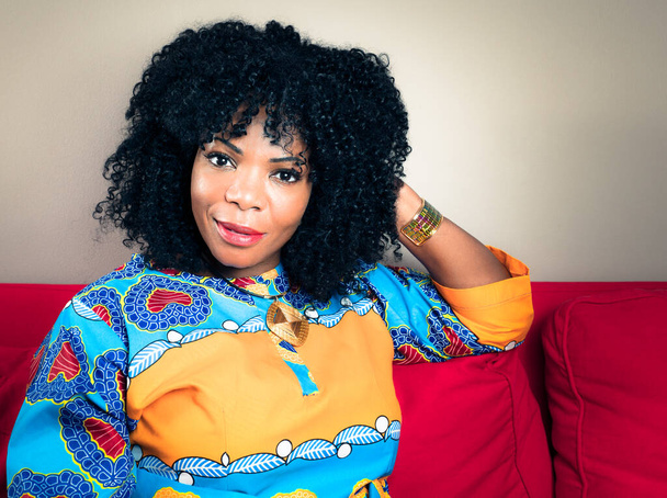 Horizontales Porträt einer lächelnden Afroamerikanerin auf einem roten Sofa - Foto, Bild