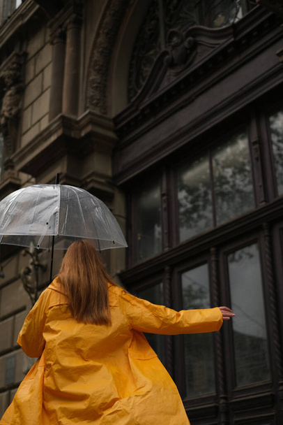 красивая женщина в жёлтом плаще ходит по городу с прозрачным зонтиком под дождем. - Фото, изображение
