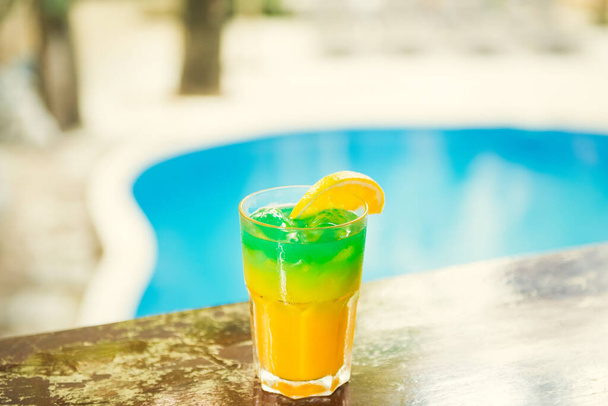 Colorful tropical cocktails on wooden bar. Mixology in pool holiday setting. Caribbean cocktails. Colorful cocktails in caribbean bar hotel - Photo, Image