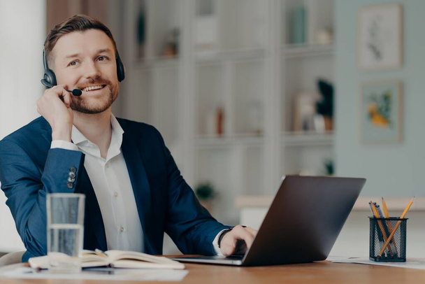 Smiling manager having online call on laptop while sitting at table in living room - Photo, Image
