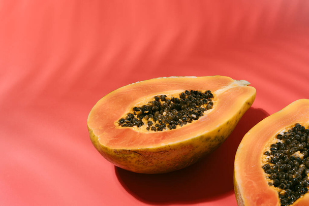 Świeża papaja z czarnymi nasionami na czerwonym tle z cieniami liści kokosowych w lecie. wakacje i koncepcja przyrody. przestrzeń kopiowania. - Zdjęcie, obraz