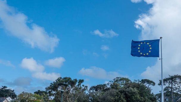 Az Európai Unió zászlója lobogott az égen: Felvételek egy európai uniós zászlóról és zászlórudról, amely a szélben fúj egy fényes, napos nyári napon, amelyet a franciaországi Pornóban készítettek 2021. május 21-én - Fotó, kép