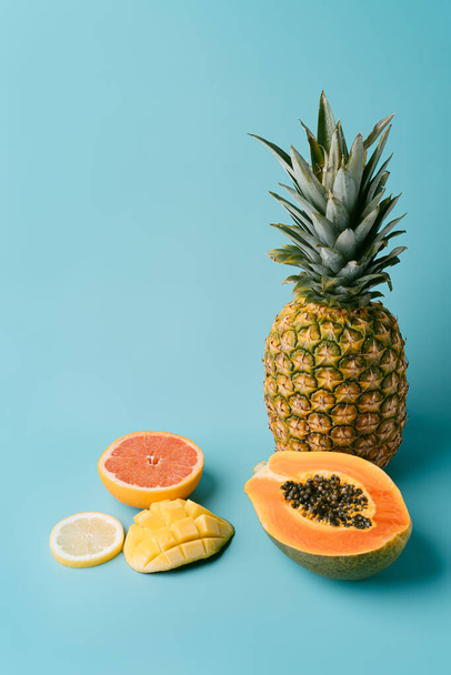 Fresh exotic fruits on blue background - papaya, mango, pineapple, lemon, grapefruit. Summer concept and healthy food. vertical image with copy space - Foto, Imagen