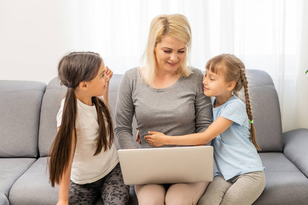 Улыбающаяся мать с маленькими детьми, использующая ноутбук дома - Фото, изображение