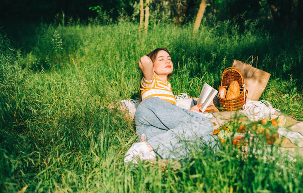 Young woman reading book outdoors, in natural park on picnic, lying on a picnic blanket and enjoying summer weather. - Foto, afbeelding
