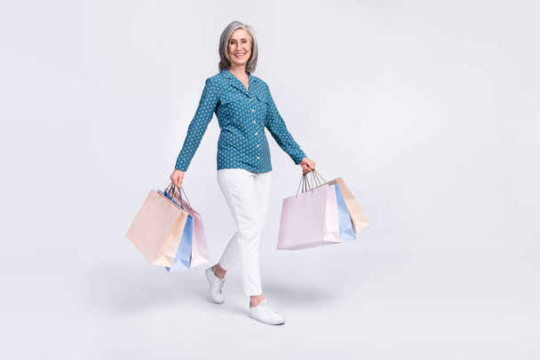 Full length body size view of attractive cheerful middle-aged lady carrying bags isolated over gray light pastel color background - Foto, imagen