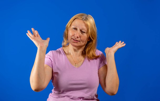 Mooie vrouw poseren lachend met handpalmen omhoog als een zingen van niet begrijpen iets geïsoleerd op blauwe studio achtergrond. Twijfelachtig concept - Foto, afbeelding